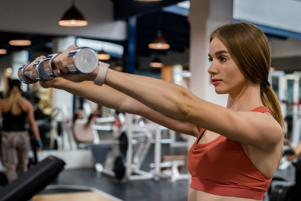 Beautiful young woman trains deltoid in gym