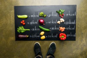partial view of man standing near fresh vegetables and calories table, healthy lifestyle concept