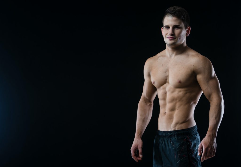 Young and fit male model posing his muscles looking straight to camera